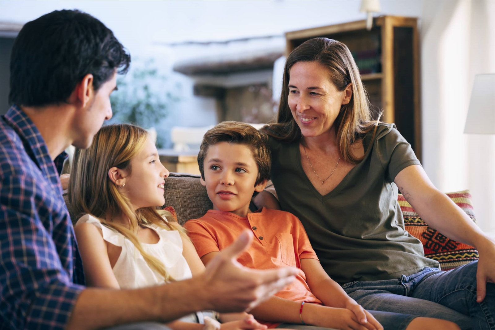  A family of four is sitting on a couch in their living room, talking.